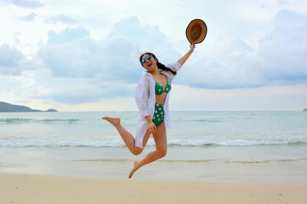 Woman jumps joyfully on a Phuket beach in summer, embodying carefree vacation spirit.